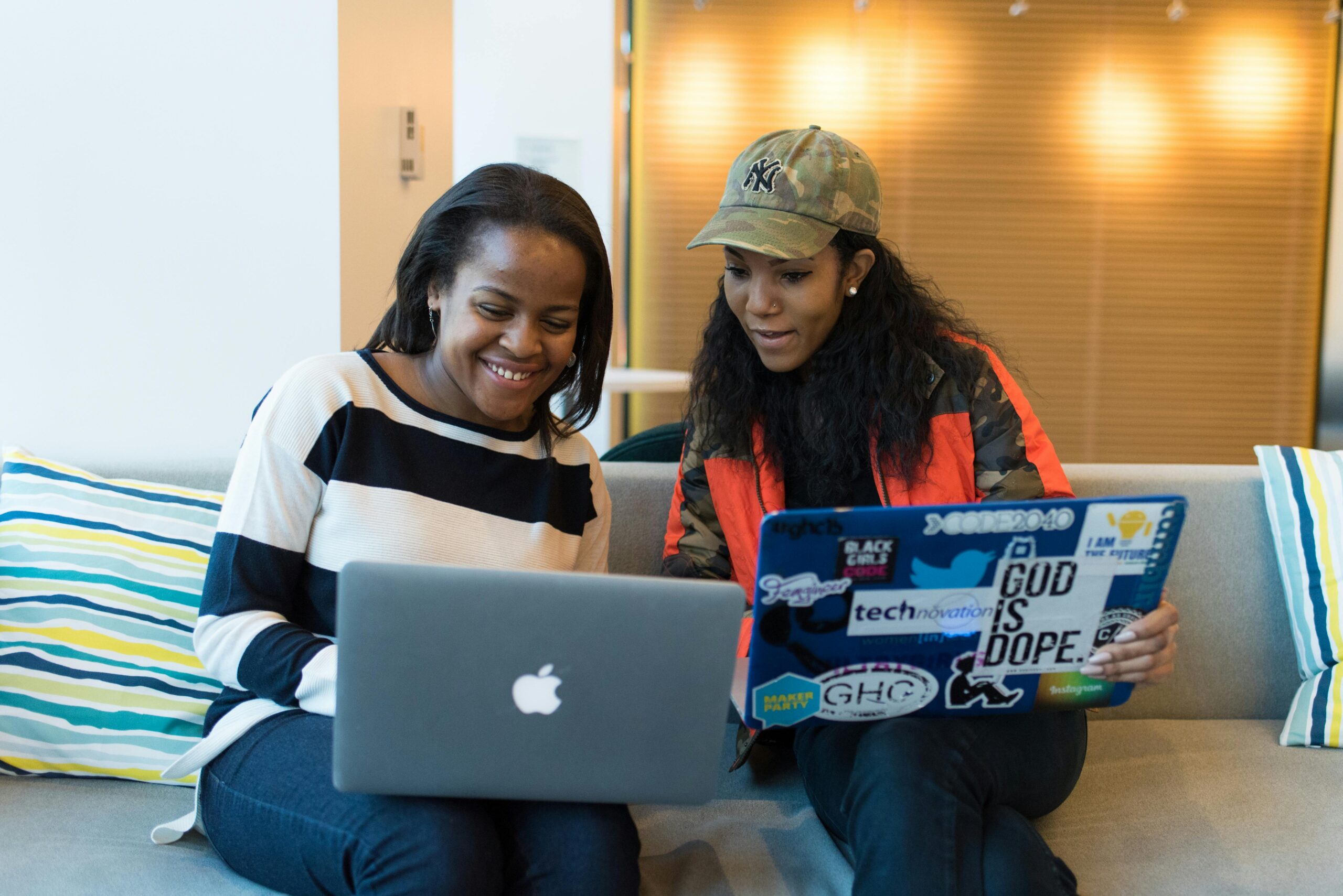 Two women engaged in collaborative work on laptops in a contemporary office setting.