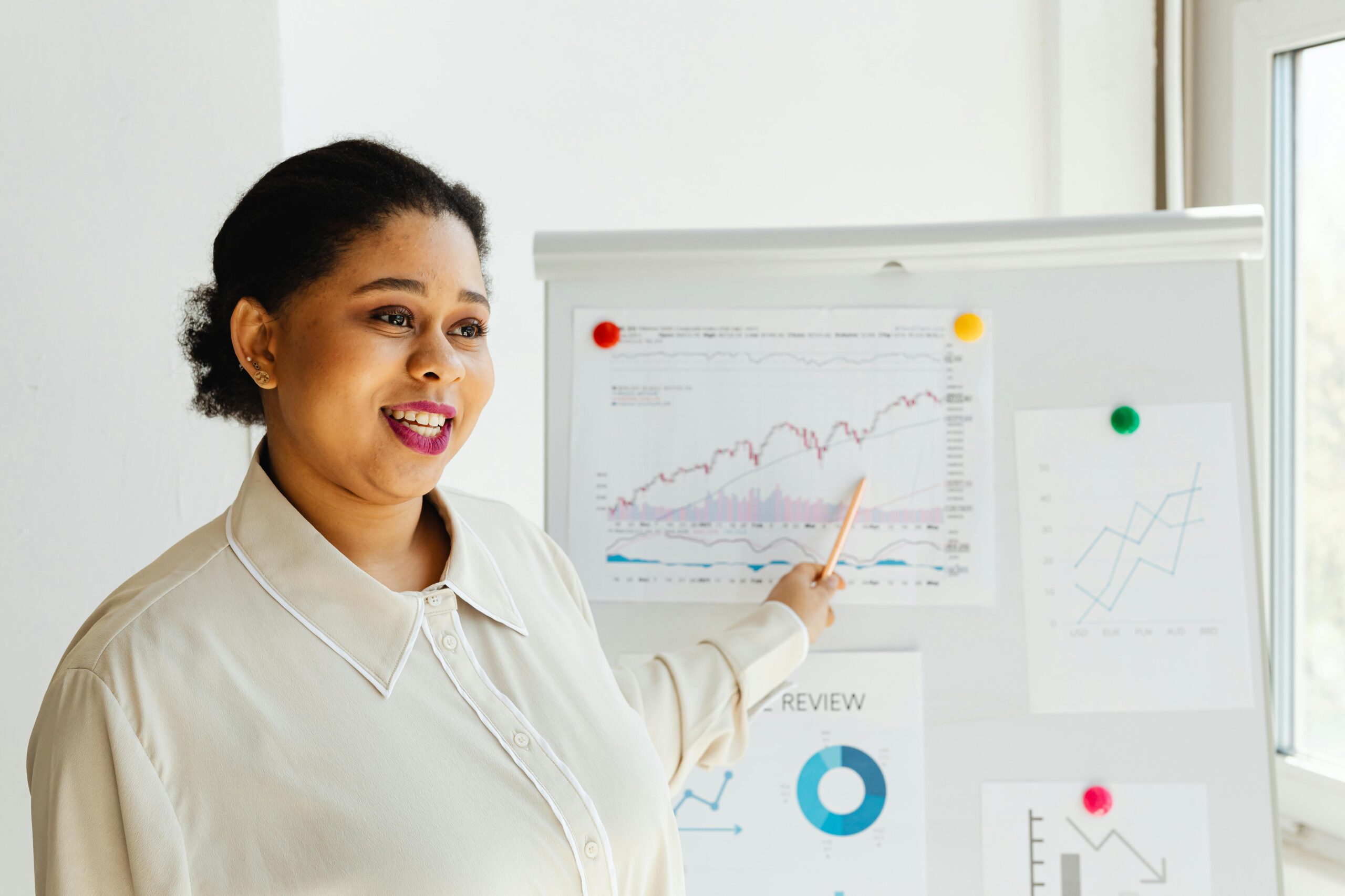 African American woman smiling while presenting financial charts on whiteboard.